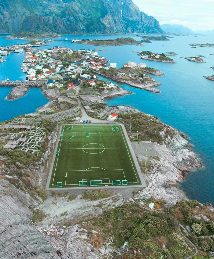 A breathtaking aerial view of a soccer field in Lofoten Islands, Vågan, Norway surrounded by stunning seascape and mountains.